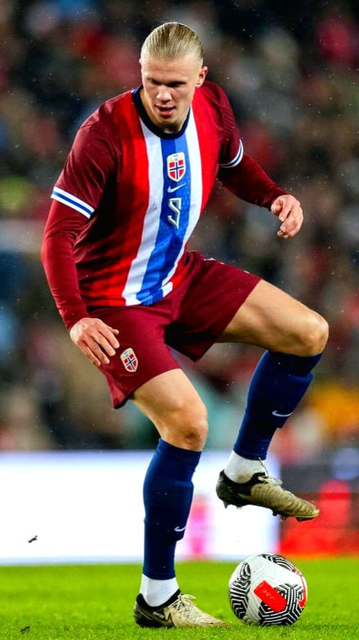 A male soccer player in a red and blue Norway uniform with the number 9 controls a soccer ball on the field during a match, streamed live on Latino IPTV.